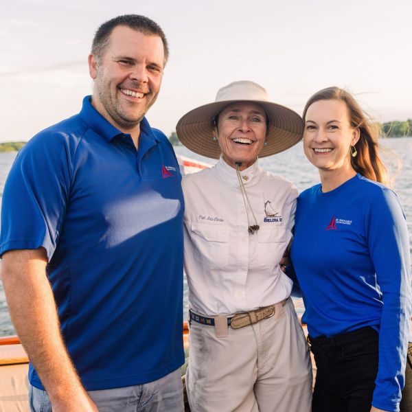 Three people smiling on a boat with water in the background.