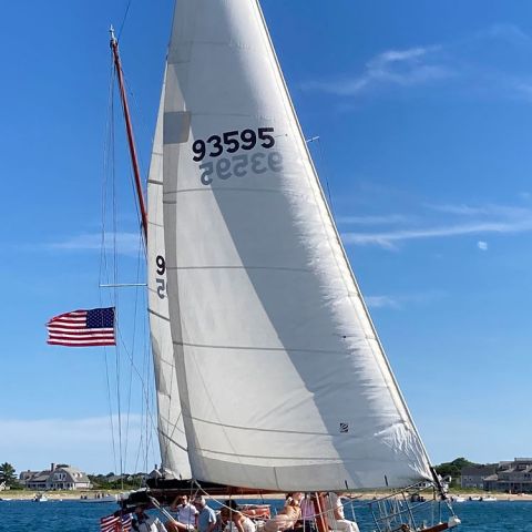Sailboat with American flag sailing on blue water under clear sky.