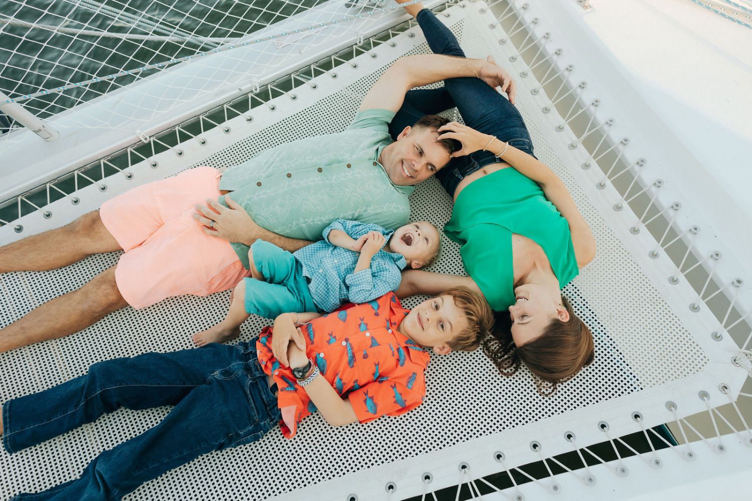 Family of four lying on a netted platform, smiling and enjoying a relaxed moment.