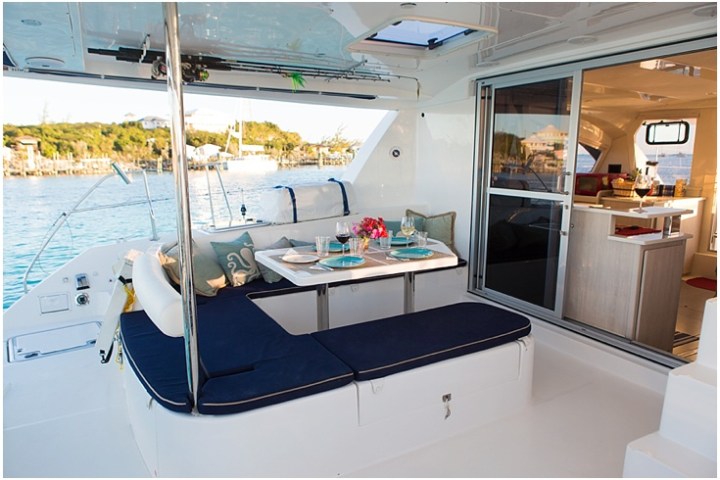 Outdoor yacht dining area with cushioned seats and table set for two, overlooking water and shoreline.