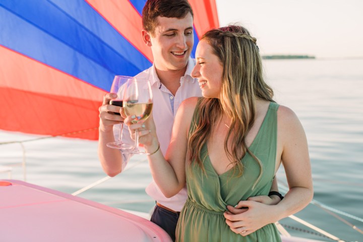 Couple toasting with wine glasses on a boat with a colorful sail in the background.