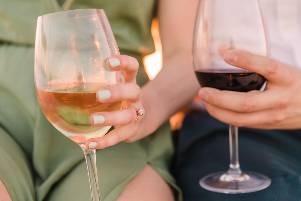 Two people holding glasses of white and red wine, one wearing a ring.