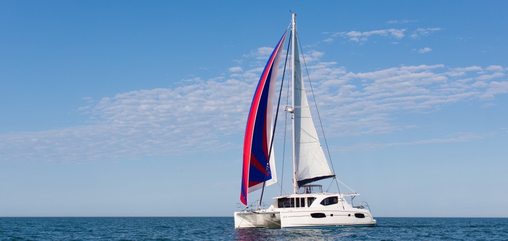 White catamaran with red and blue sail on open sea under a clear blue sky.