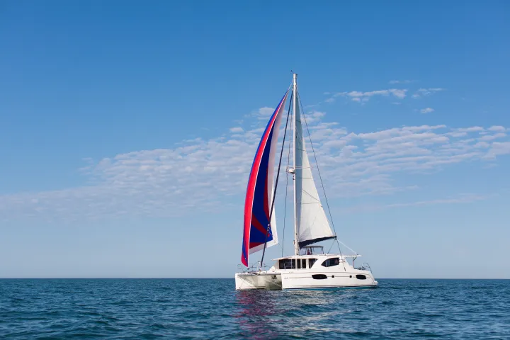 Catamaran with colorful sail on calm sea under clear blue sky.