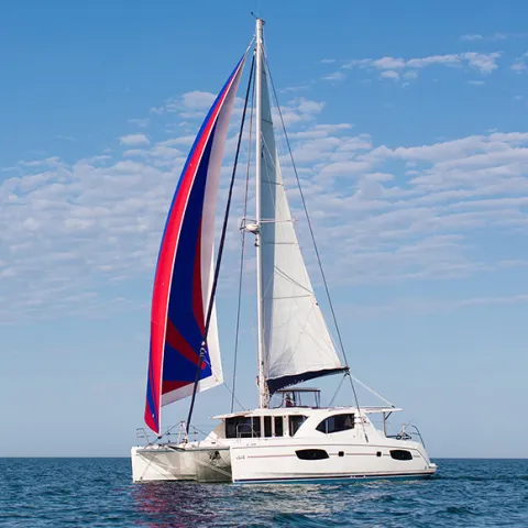 Catamaran sailing with red and blue spinnaker on a clear day at sea.