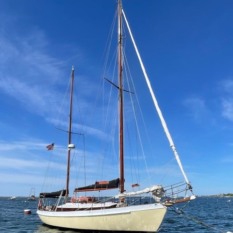 Sailboat with two masts on water under blue sky with a small flag.