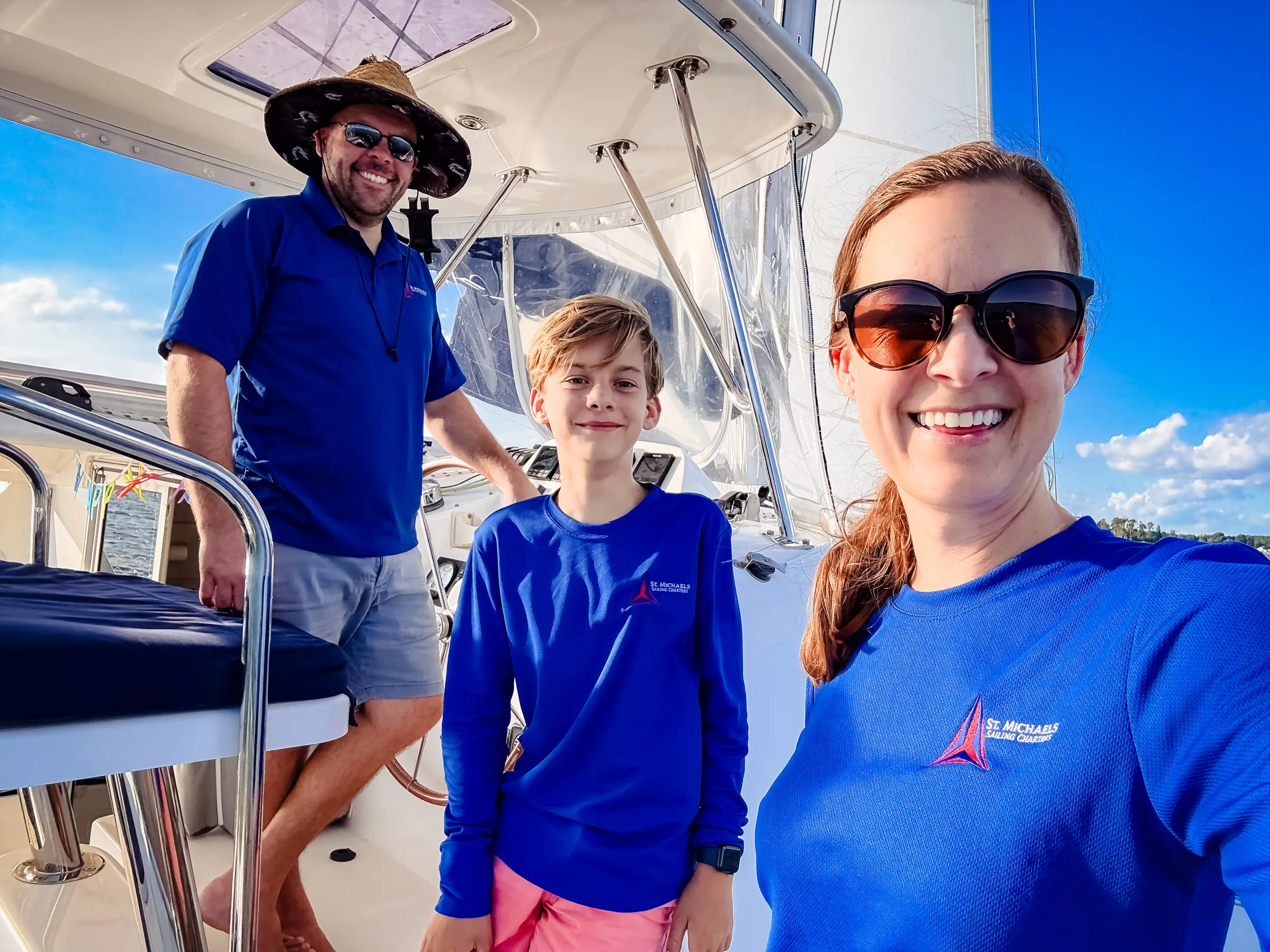 Three people smiling on a boat deck wearing blue shirts and sunglasses.