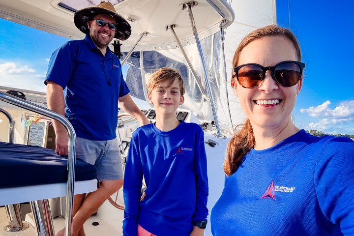 Three people smiling on a boat deck wearing blue shirts and sunglasses.