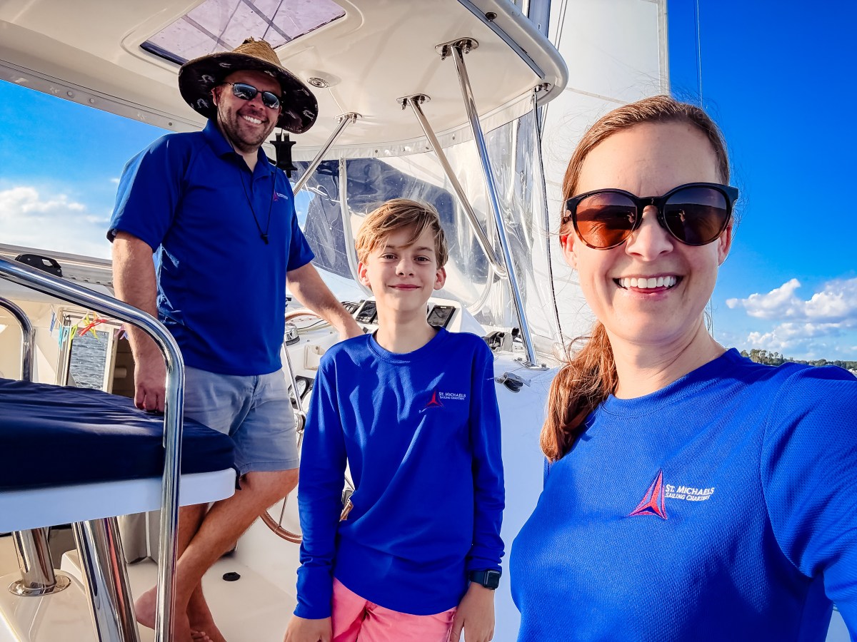 Three people smiling on a boat deck wearing blue shirts and sunglasses.