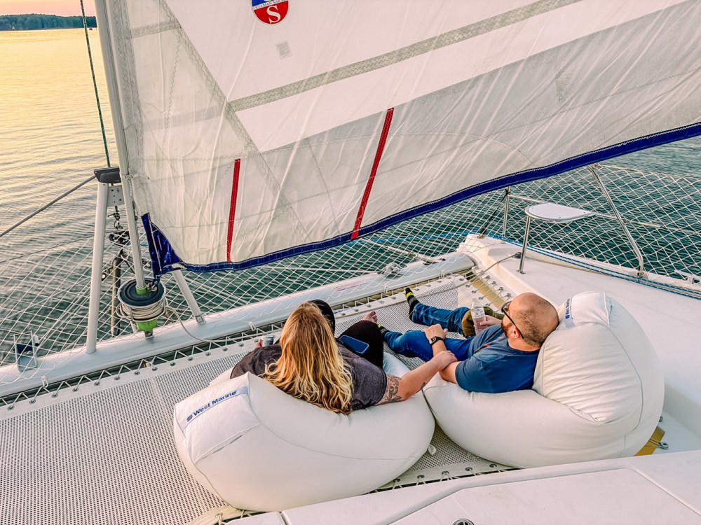 Two people relaxing on bean bags on a sailboat deck, holding hands at sunset.