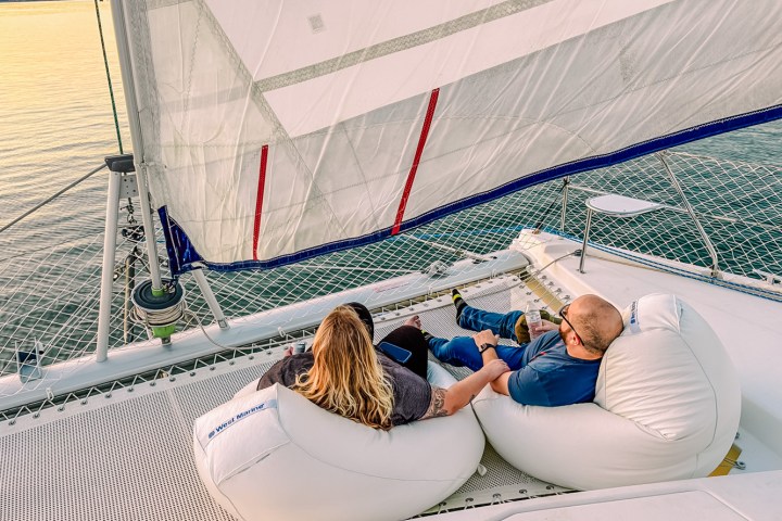 Two people relaxing on bean bags on a sailboat deck, holding hands at sunset.