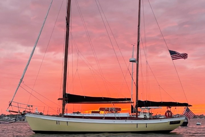 Sailboat on water at sunset with pink and orange sky, American flag visible.