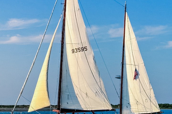 Yellow sailboat with three sails and people onboard in a sunny, blue sky setting.