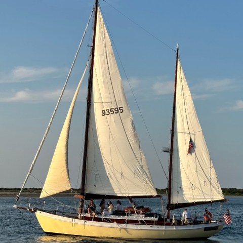 Yellow sailboat with white sails and people aboard on a sunny day.