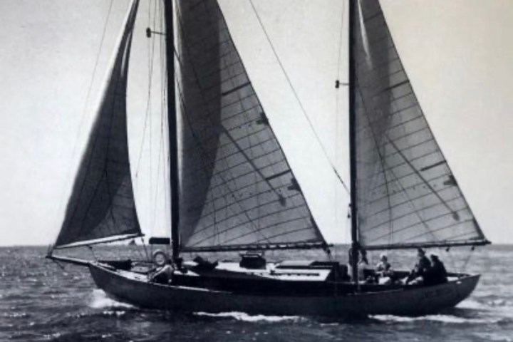Black and white photo of a sailboat with two sails on the water.