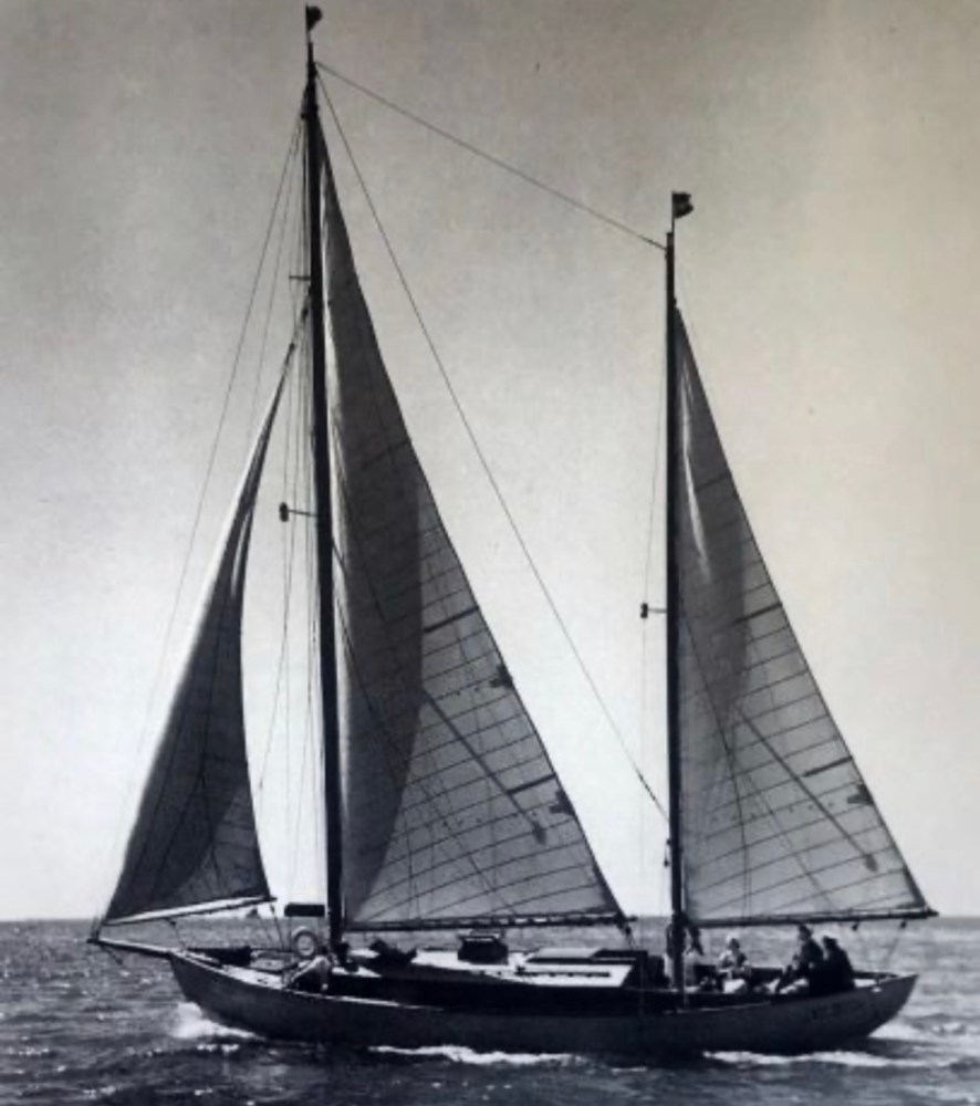 Black and white photo of a sailboat with two sails on water.