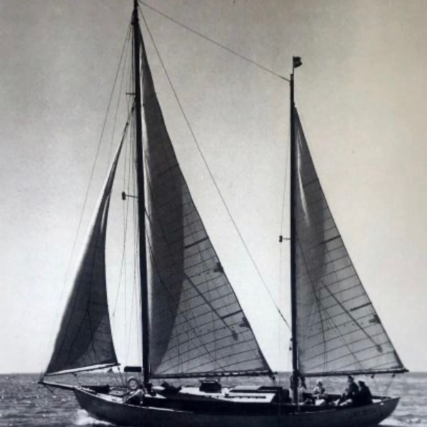 Black and white photo of a sailboat with two sails on water.