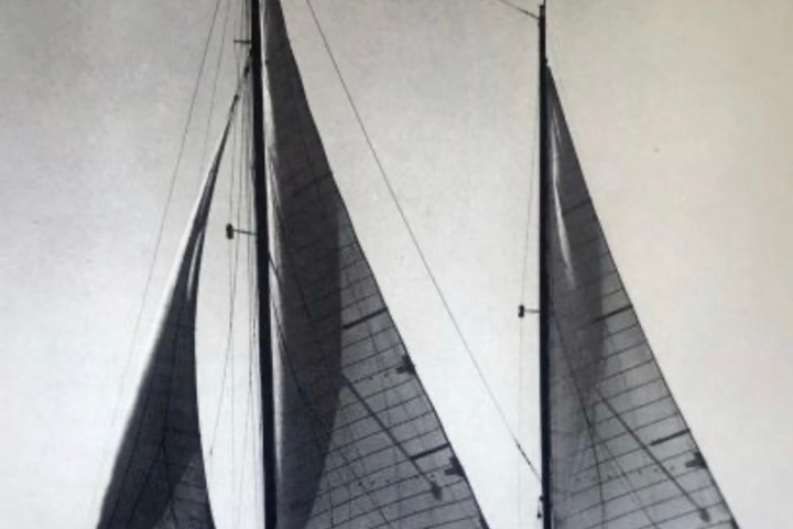 Black and white photo of a sailboat with two sails on water.