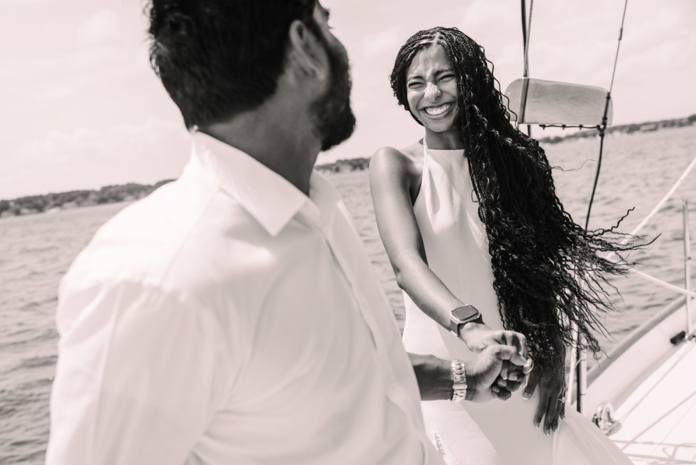 Smiling couple holding hands on a sailboat on a sunny day.