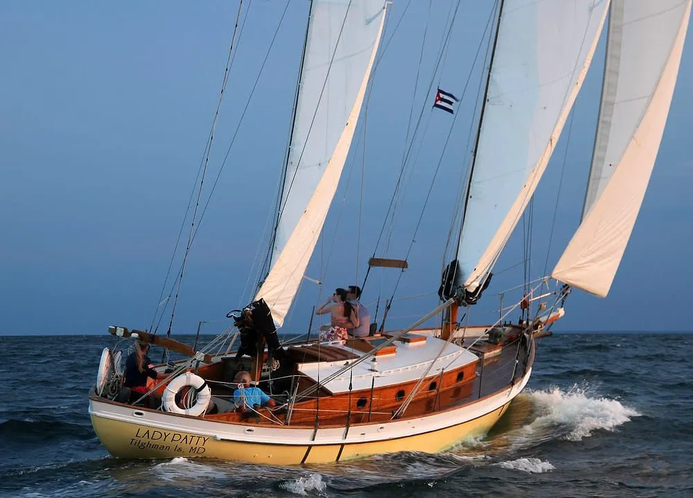 Sailing boat with white sails on the ocean, carrying people and named 'LADY PATTY'.