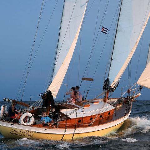 Sailing boat with white sails on the ocean, carrying people and named 'LADY PATTY'.
