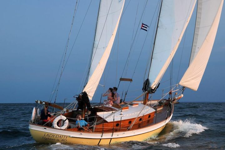 Sailing boat with white sails on the ocean, carrying people and named 'LADY PATTY'.