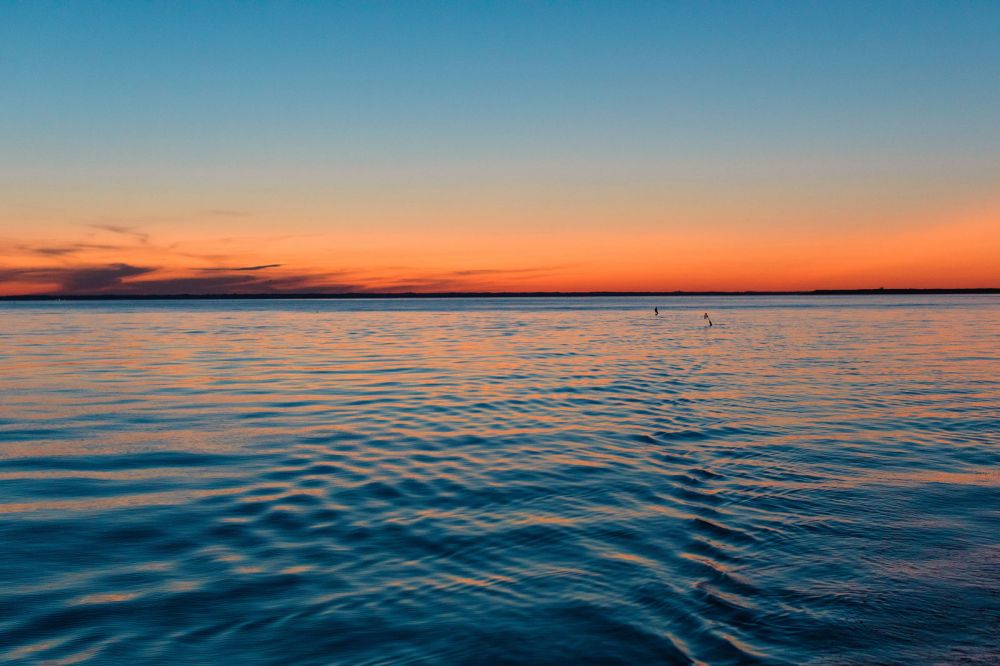 Calm ocean at sunset with orange sky and distant horizon.