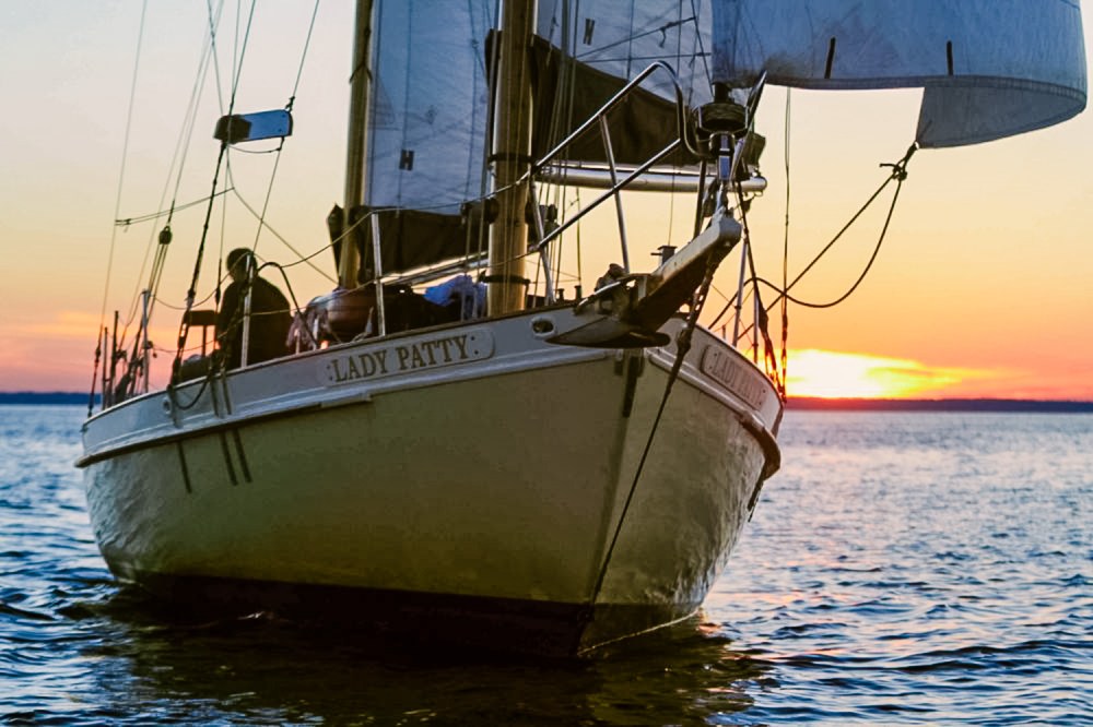 Sailboat named Lady Patty on the water at sunset with sails set.