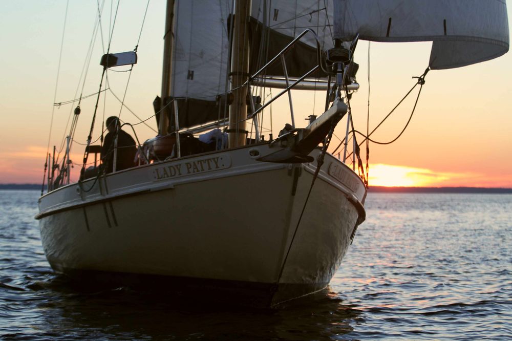 Sailboat on water at sunset with visible sails and a person aboard.