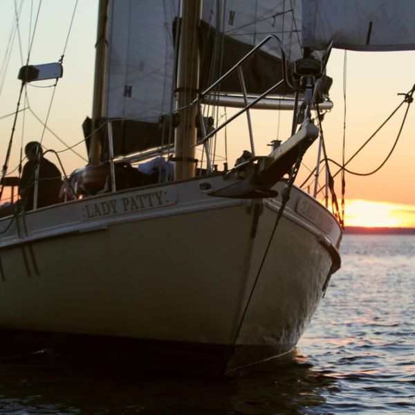 Sailboat on water at sunset with visible sails and a person aboard.
