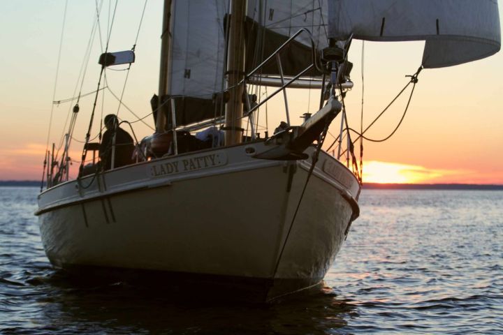 Sailboat on water at sunset with visible sails and a person aboard.