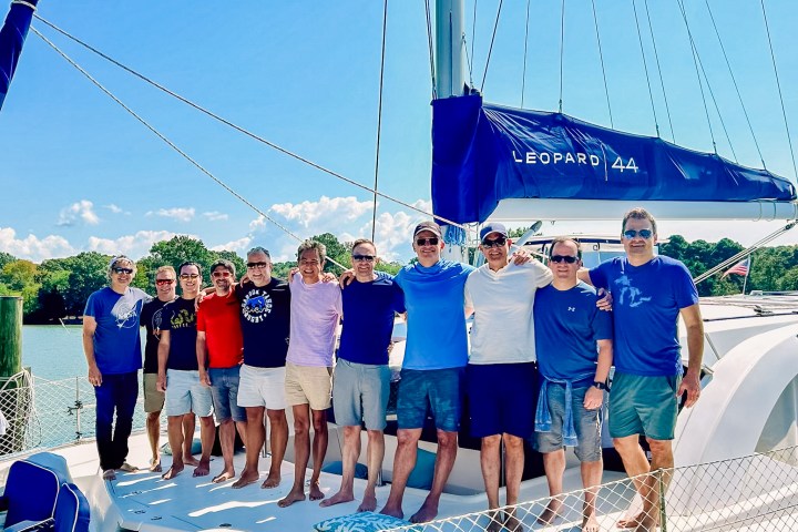 Group of 10 men posing on a Leopard 44 catamaran in a sunny outdoor setting.