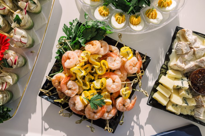 Variety of appetizers including shrimp skewers, deviled eggs, and cheese platter on a table.