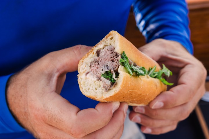 Person holding a sandwich with meat and lettuce in a baguette.