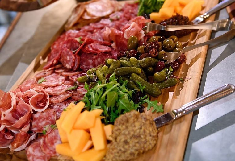 A charcuterie board with meats, cheeses, olives, gherkins, and mustard.