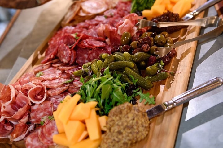 A charcuterie board with meats, cheeses, olives, gherkins, and mustard.