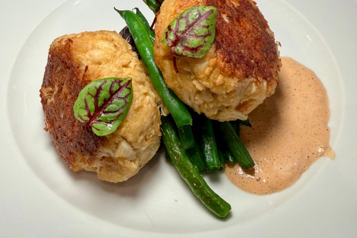 Two crab cakes on green beans with sauce and garnish on a white plate.