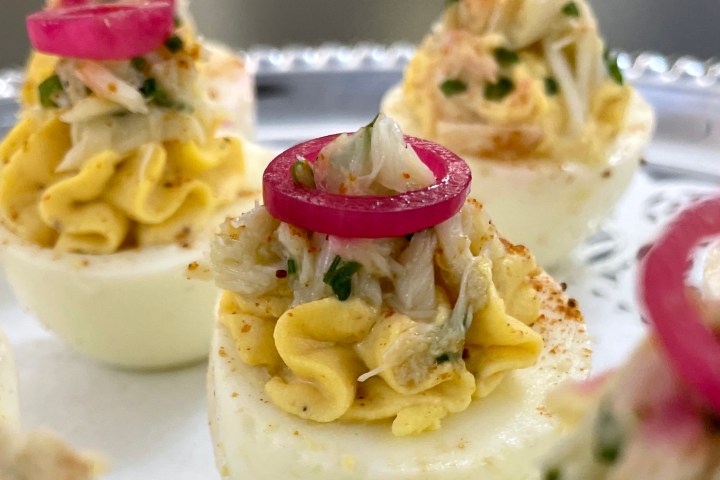 Deviled eggs topped with crab meat and pickled onions on a tray.