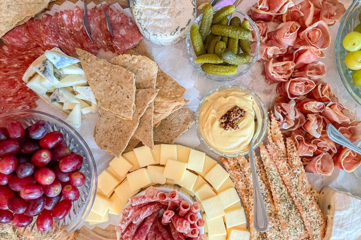 Charcuterie board with meats, cheeses, grapes, pickles, crackers, and mustard dip.
