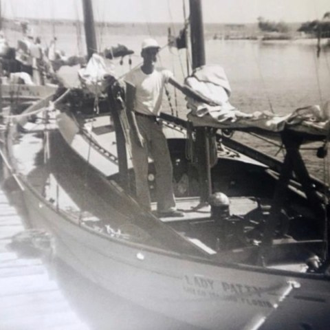 Vintage photo of a man standing on a sailboat docked at a wooden pier.
