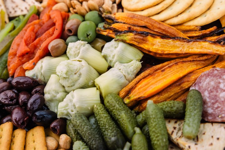 Assorted antipasto platter with olives, artichokes, peppers, crackers, and cured meats.