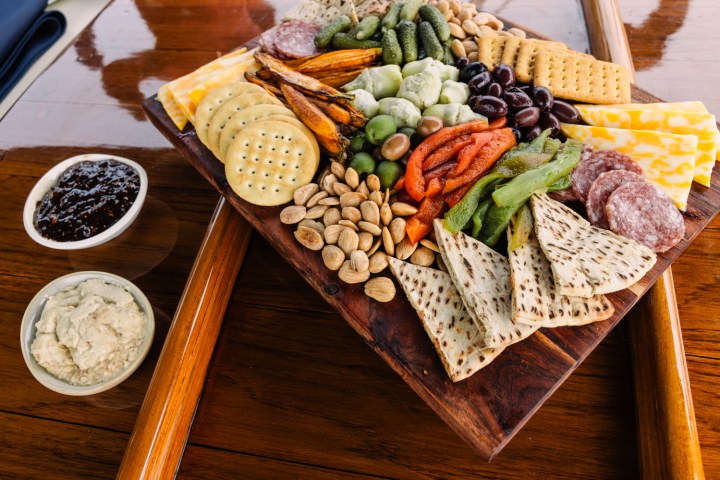 Charcuterie board with crackers, cheese, meats, nuts, olives, pickles, and dips.
