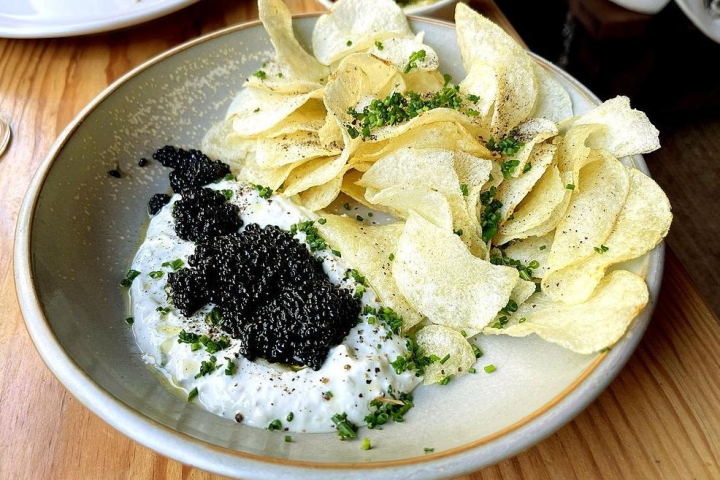 Chips with caviar and cream cheese garnished with herbs in a bowl.