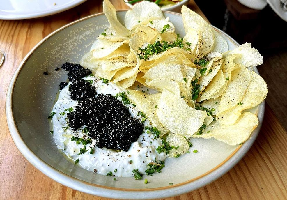 Chips with caviar and cream cheese garnished with herbs in a bowl.