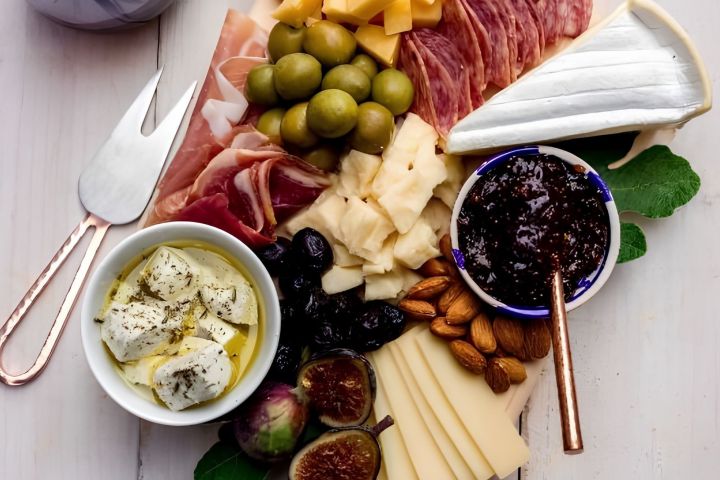 Charcuterie board with cheeses, meats, olives, figs, almonds, and a cup of fig jam.