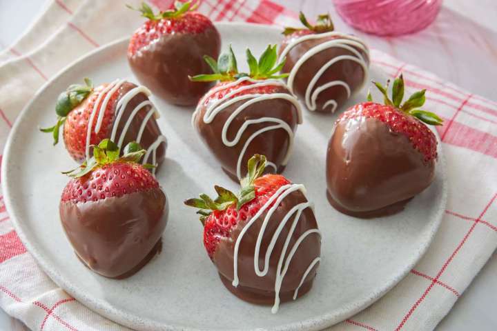 Plate of chocolate-covered strawberries with white drizzle.