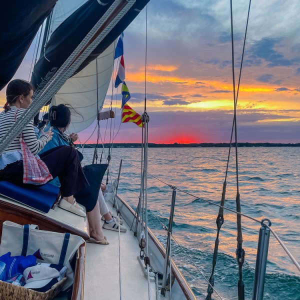 People on a sailboat at sunset with colorful sky over the water.