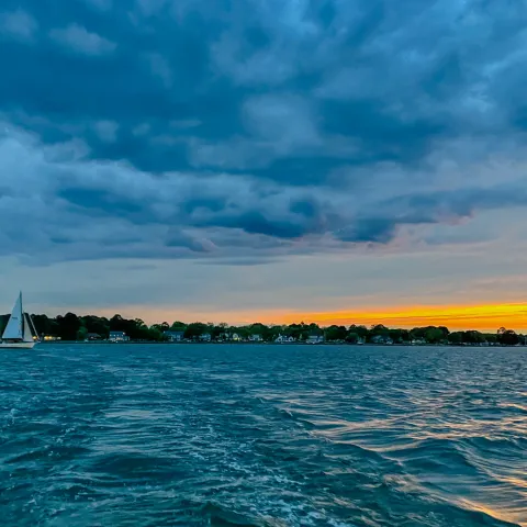 Sailboat on a lake at sunset with dramatic clouds and orange horizon.