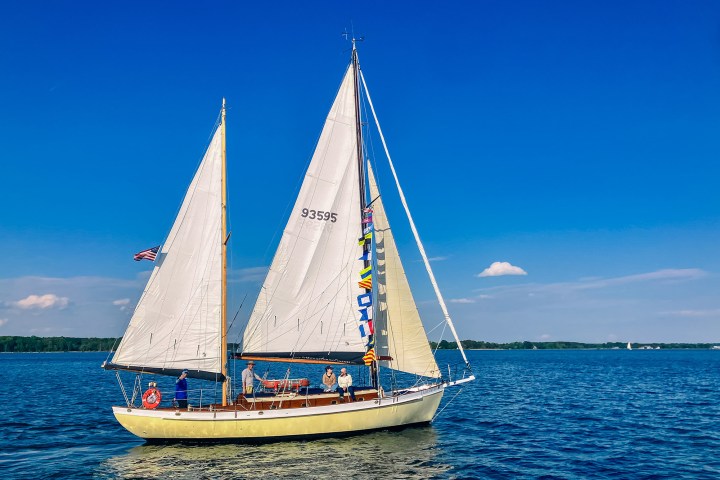 Sailboat with colorful flags on a calm lake under a clear blue sky.