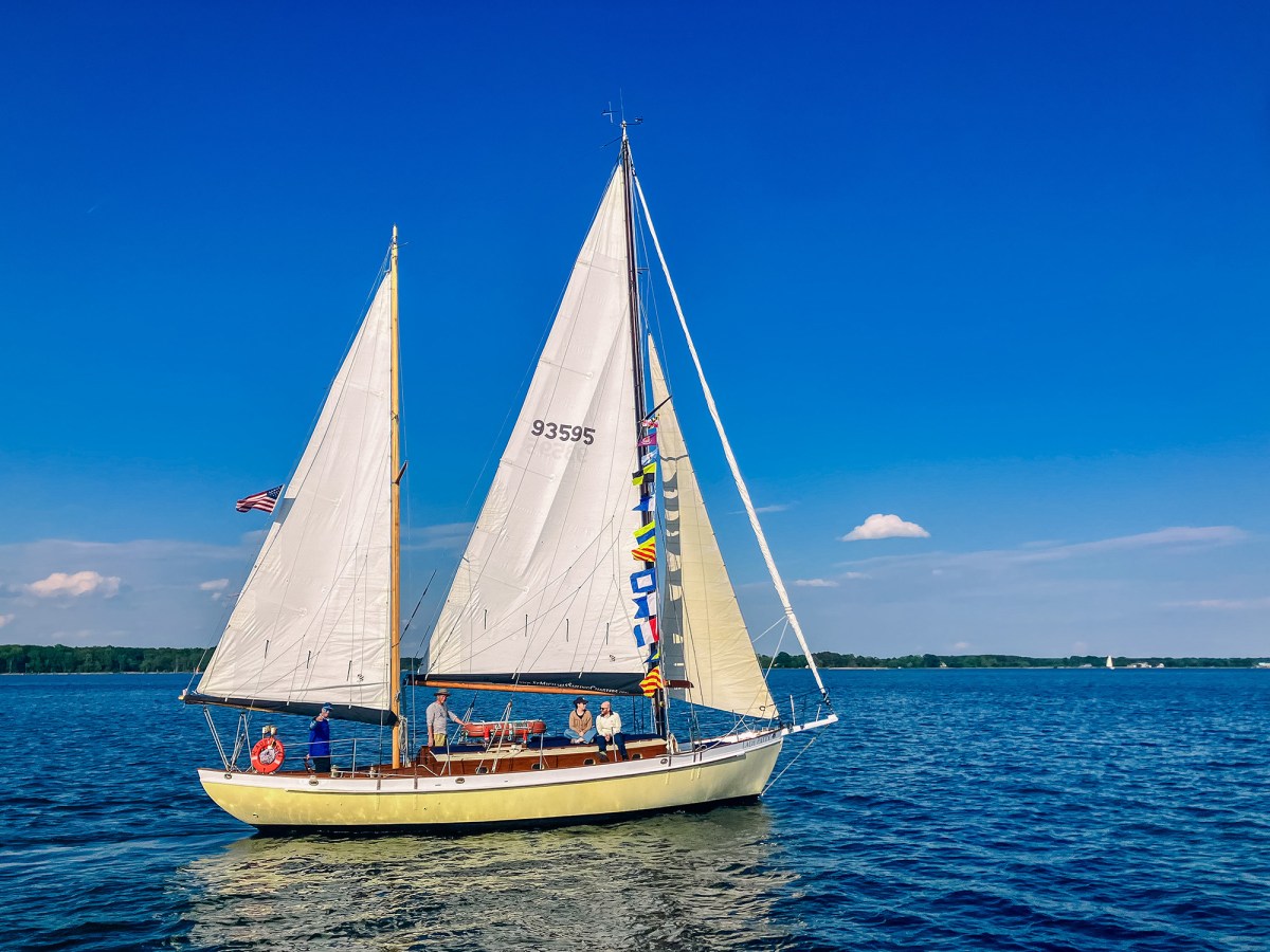 Sailboat with colorful flags on a calm lake under a clear blue sky.
